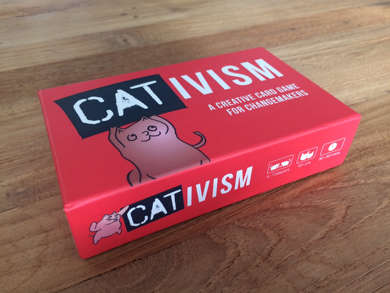 a red box of a card game called: cativism showing a comic cat holding a sign