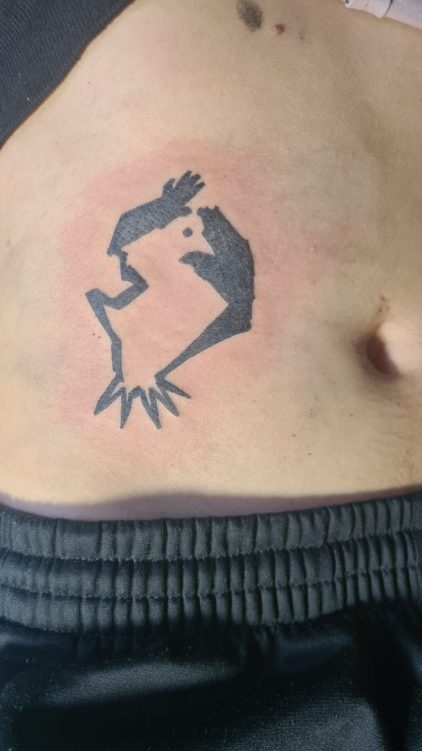 A belly tattoo in black shapes. Two hands, the empty parts forming a bird.