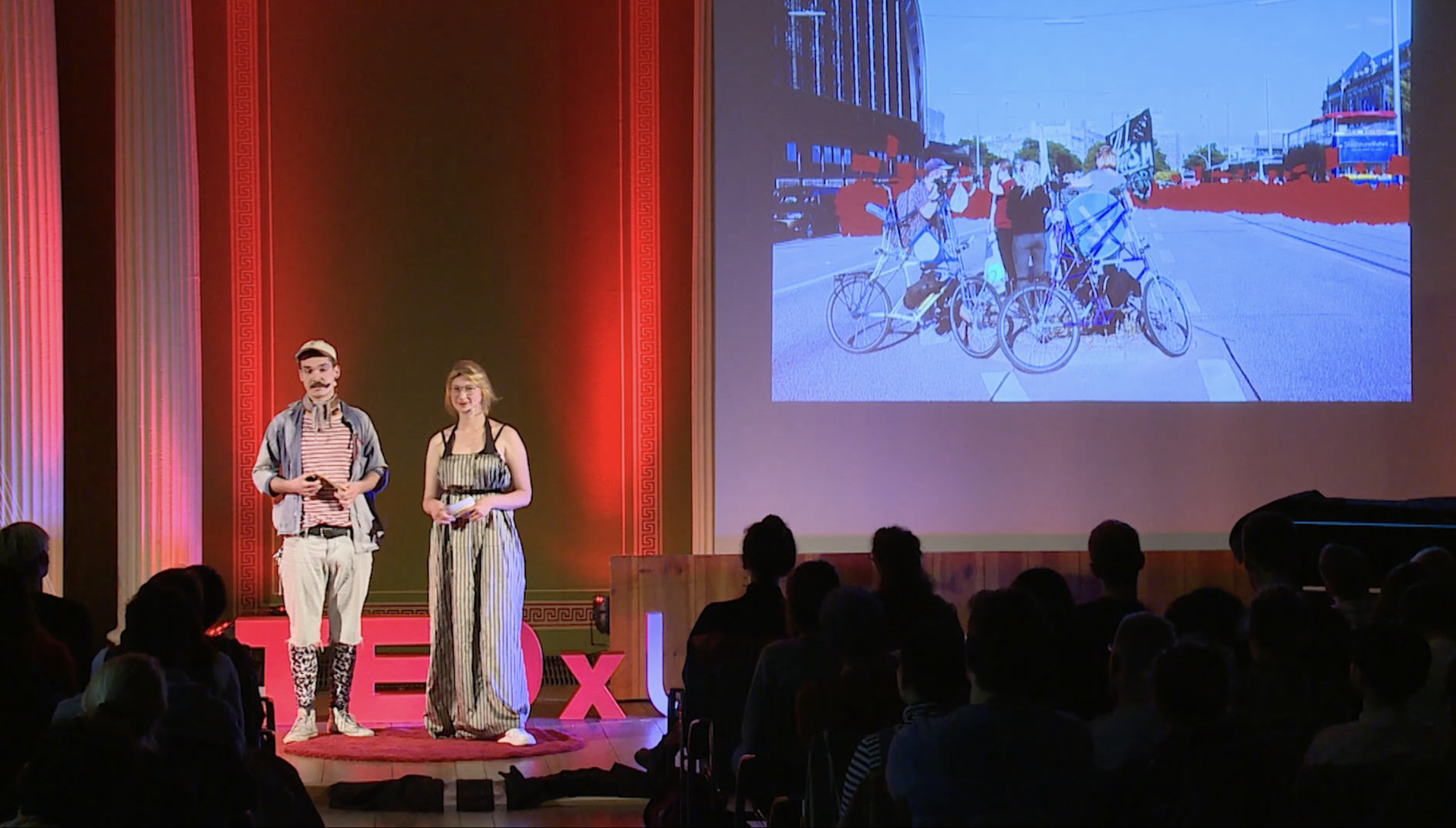 Two people giving a TEDx talk about tallbikes