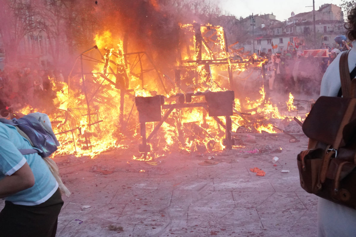 A huge bonfire surrounded by people on a town square.